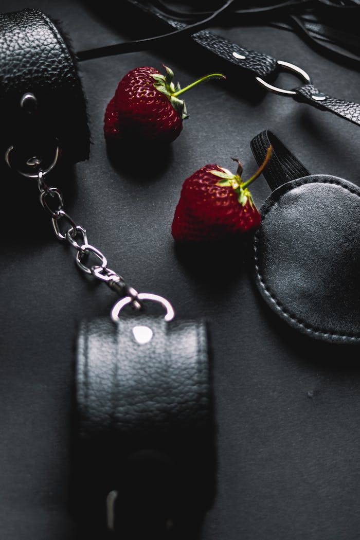 Close-up of leather accessories and strawberries on a dark background, blending textures and colors.